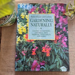 May include: A gardening book titled "Gardening Naturally" by Better Homes and Gardens. The cover features a vibrant floral arrangement with yellow, pink, and red flowers. The book's subtitle reads: "A guide to growing chemical-free flowers, vegetables, and herbs."