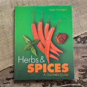 May include: A cookbook titled "Herbs & Spices: A Gourmet's Guide" with a green cover. The cover features vibrant red chili peppers, fresh basil, and a pile of ground spices. The author's name, Karen Farrington, is at the top.