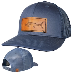 May include: A navy blue trucker hat with a brown leather patch featuring a marlin illustration. The hat has a mesh back and a curved brim.