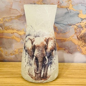 May include: A white ceramic vase with a textured surface features a watercolour illustration of an elephant. The elephant is depicted in shades of brown and grey, with a light blue background.