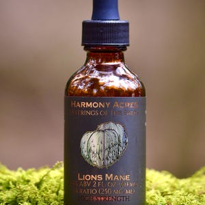 May include: A brown glass bottle with a dark label featuring the text "Lions Mane" and a botanical illustration. The bottle has a black cap and a blue dropper. The bottle is 2 fl oz (60 ml).