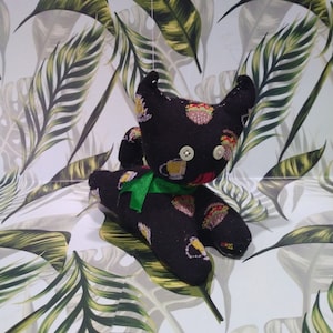 May include: Black and green sock monkey toy with a green bow tie. The monkey is sitting on a white background with a green tropical leaf pattern.