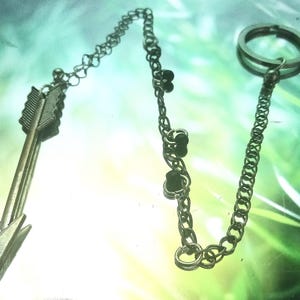 May include: A silver arrow charm attached to a silver chain with black beads. The chain has a silver ring at the end.