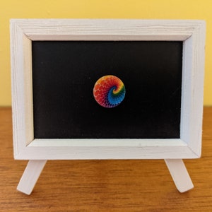May include: A white easel with a black chalkboard and a rainbow colored spiral design on a white circle.
