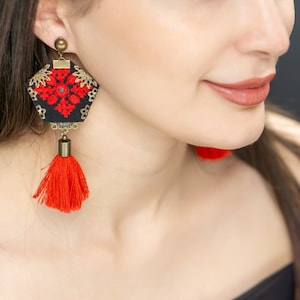 May include: A pair of black and red earrings with a geometric design and a tassel. The earrings are made of fabric and have a gold-colored metal accent.