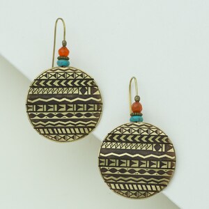 Peut inclure: Une paire de boucles d'oreilles dorées avec un motif rond et géométrique. Les boucles d'oreilles ont un accent de perles turquoise et orange.