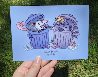 Peut inclure: Une illustration bleue et violette d'un raton laveur et d'une opossum dans des poubelles. Le raton laveur porte un bandeau jaune et l'opossum porte une boucle d'oreille en forme de cœur. Le texte "trash friends for life" est sous l'image.