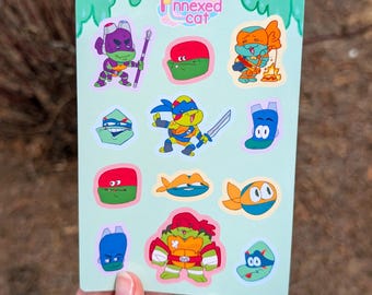 May include: A light green sticker sheet featuring various cartoon illustrations of turtle characters in masks, including full-body poses and headshots. The top center displays the text "Annexed cat" with a small star icon. The designs include vibrant colors like purple, red, orange, and blue.