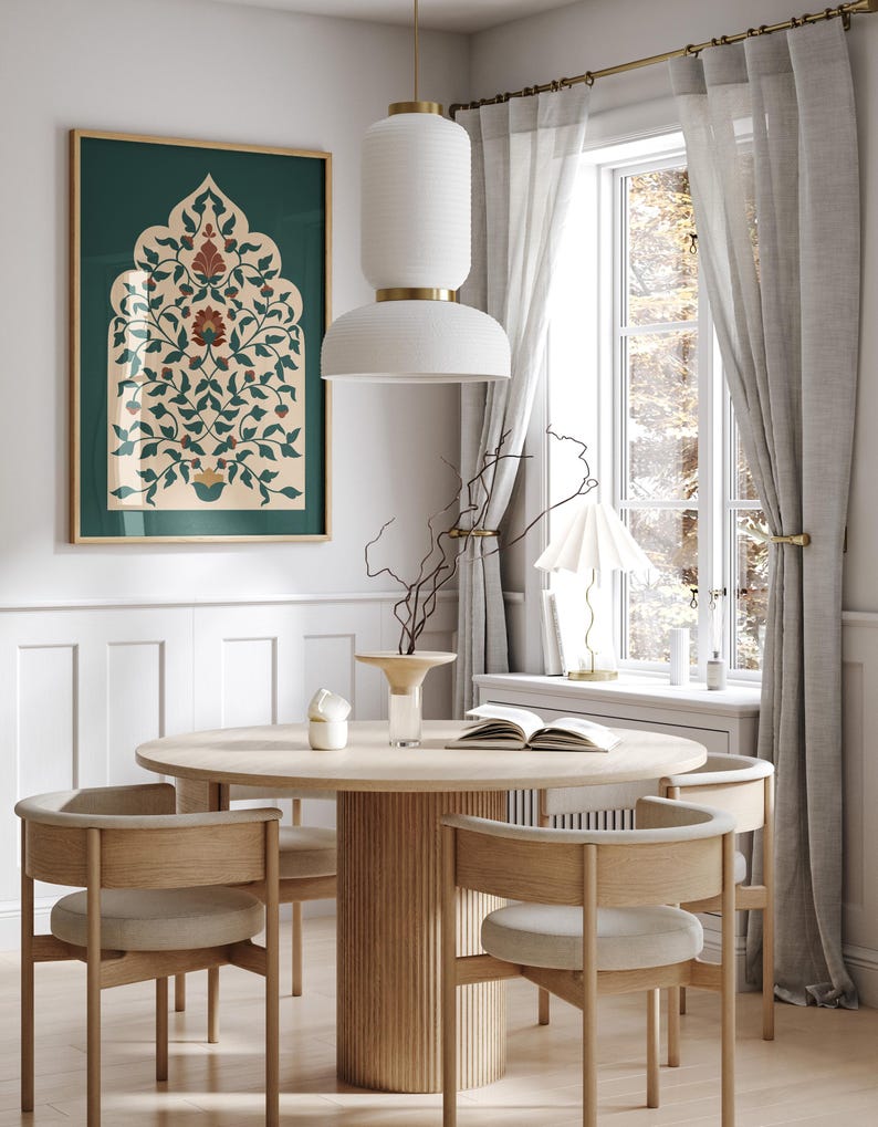 May include: A dining room scene featuring a round wooden table with four chairs. A framed artwork with a green background and floral design hangs on the wall. A white pendant light hangs above the table, and a window with sheer curtains is visible.