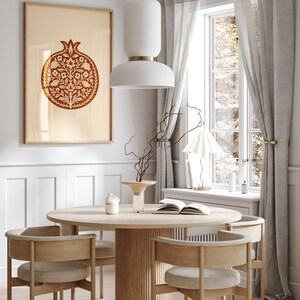 May include: A dining room scene featuring a round wooden table with four chairs. A framed artwork with a pomegranate design hangs on the wall. A white pendant light hangs above the table, and a window with sheer curtains is visible.