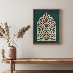 May include: A framed print featuring an ornate floral design in shades of cream, green, and red. The artwork is set against a dark green background and framed in a wooden border. The print is displayed on a wooden shelf.