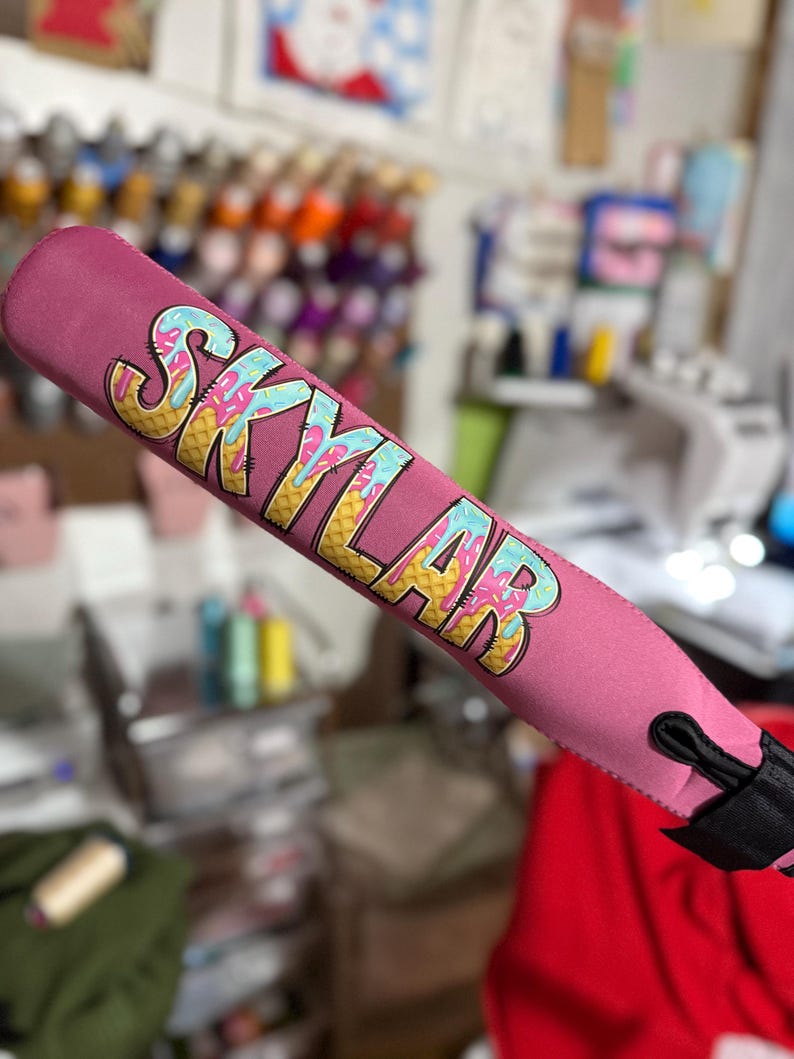 Puede incluir: Cubierta de manillar de scooter rosa con un dise&ntilde;o de cono de helado colorido y el nombre "Skylar" impreso en &eacute;l.