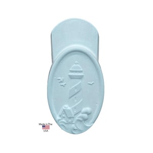 May include: A light blue, oval-shaped magnet featuring a lighthouse design. The lighthouse is embossed with details like the tower, roof, and waves. The text "Made in the USA" is printed on the bottom.