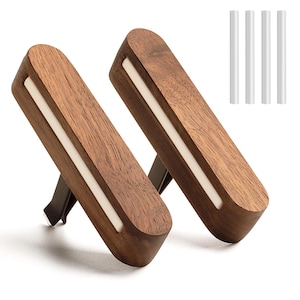 Puede incluir: Dos ambientadores de coche de madera marrón con una inserción rectangular blanca. Los ambientadores tienen un clip de metal oscuro. También son visibles cuatro palitos perfumados blancos.