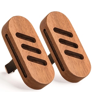 May include: Two oval-shaped wooden car air freshener clips featuring a natural brown wood grain finish. Each piece has three diagonal ventilation slots cut into the front surface, revealing a dark brown felt insert behind the wooden exterior.