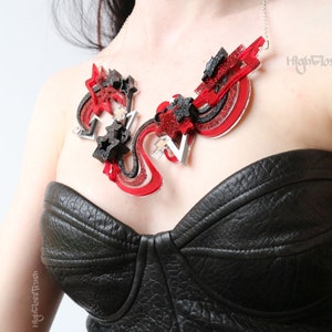 May include: A red, black, and silver statement necklace with a geometric design. The necklace features stars, swirls, and abstract shapes. The text "High Gloss Trash" is visible on the right side of the image.