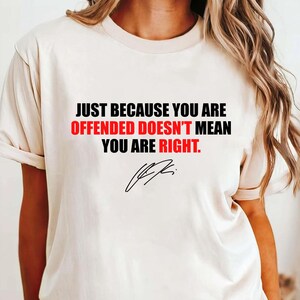 Op de afbeelding: Crèmekleurig T-shirt met de tekst "JUST BECAUSE YOU ARE OFFENDED DOESN'T MEAN YOU ARE RIGHT." in zwart en rood. Inclusief een handtekening in zwart. Het shirt heeft korte mouwen en een ronde hals.