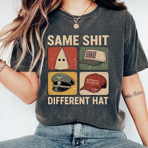 Könnte beinhalten: Dunkelgraues T-Shirt mit dem Text "SAME SHIT DIFFERENT HAT". Das Shirt zeigt vier Bilder: eine weiße Kapuze, einen Hut mit einer Konföderierten Flagge, einen Militärhut mit einem Totenkopf und einen roten "Make America Great Again" Hut.