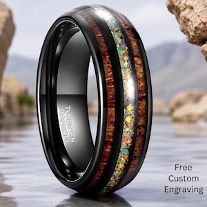 May include: A black tungsten carbide ring featuring a central inlay of iridescent crushed opal flanked by two bands of dark brown wood grain. The interior of the band is engraved with the text Tungsten Carbide and Free Custom Engraving.