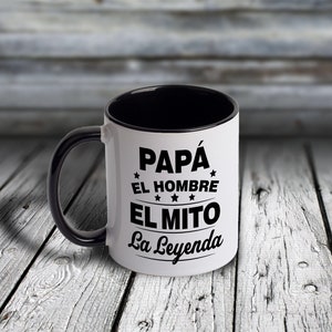 May include: White ceramic mug with a black interior and handle. The mug has black text that reads "Papá El Hombre El Mito La Leyenda" with stars around the text.