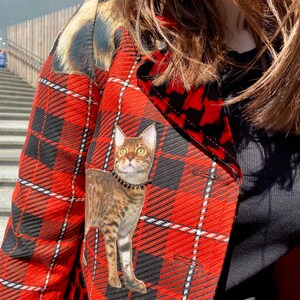 May include: A red and black plaid jacket with a cat applique. The cat is brown and black with a black collar.