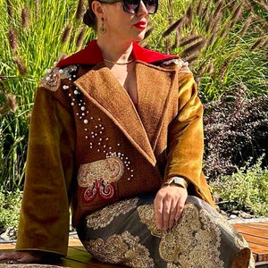 May include: A brown velvet jacket with a red collar and pearl embellishments. The jacket has a gold velvet sleeve and intricate embroidery on the front. The model is wearing a gold and black patterned skirt.