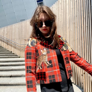 May include: A red and black plaid cropped jacket with a cat print patch and a black and white houndstooth pocket. The jacket has a black collar and a black zipper.