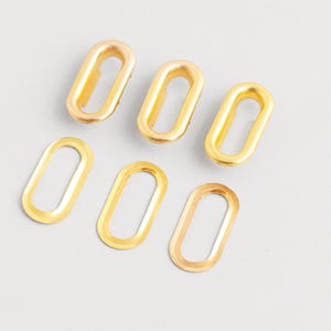 May include: Six gold-colored oval link connectors. The connectors are made of metal and have a smooth, shiny finish. The links are arranged on a light gray surface.