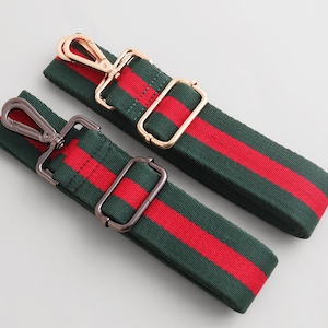 Peut inclure: Deux sangles de sac à rayures vertes et rouges avec quincaillerie métallique. Une sangle a une quincaillerie dorée et l'autre a une quincaillerie de couleur canon de fusil. Les sangles sont en tissu tissé.