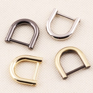 Puede incluir: Cuatro anillas en D metálicas en diferentes acabados: negro, plateado, dorado y latón antiguo. Cada anilla en D tiene un diseño curvo en forma de U con una barra recta en la parte inferior. Estas piezas de ferretería son para bolsos, cinturones u otros proyectos.