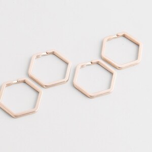 Peut inclure: Quatre porte-clés hexagonaux en or rose sont disposés sur une surface blanche. Chaque porte-clés a une fermeture à charnière. Les porte-clés sont en métal et ont une finition lisse et polie. Les porte-clés sont d'une couleur claire et chaude.