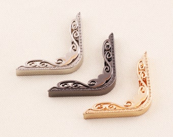May include: Three decorative metal corner brackets in silver, black, and gold. Each bracket has an ornate, scrolled design and a right-angle shape, perfect for adding a vintage touch to crafts or furniture.