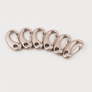 May include: Six silver-coloured oval carabiner clips arranged in a row. Each clip has a spring-loaded gate and a small hole. The clips are made of a shiny, metallic material.