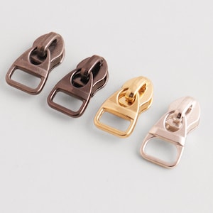 Puede incluir: Cuatro tiradores de cremallera metálicos en bronce, marrón oscuro, dorado y oro rosa. Cada tirador tiene un lazo rectangular para la fijación. Adecuado para ropa, bolsos y otros proyectos de costura.