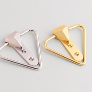 Può includere: Due pomelli decorativi per mobili. Uno è argentato, l'altro dorato. Ogni pomello presenta un'impugnatura triangolare e un elemento centrale sfaccettato a forma di diamante. I pomelli hanno due fori per le viti per il montaggio.