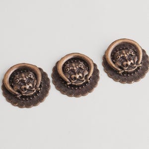 Könnte beinhalten: Drei antike Schrankgriffe aus Bronze. Jeder Griff hat ein detailliertes Löwenkopf-Design mit einem Ringgriff. Die Griffe sind auf einer dekorativen, gewellten Basis montiert. Die Hardware ist ideal, um Möbeln einen Vintage-Touch zu verleihen.