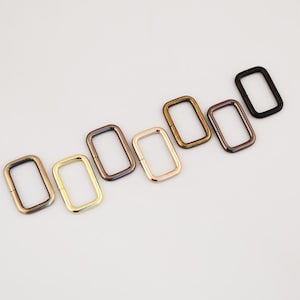 May include: Rectangular metal buckles in various colors, including gold, bronze, and black. The buckles are arranged diagonally, showcasing their different finishes. Ideal for bag straps or other craft projects.