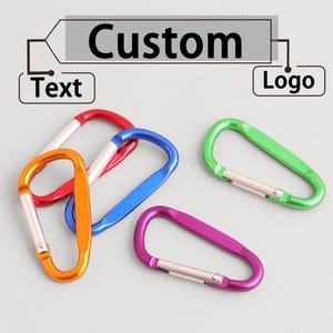 以下が含まれることがあります： 赤、オレンジ、青、緑、紫のカラビナクリップのコレクション。「Custom」の文字がクリップの上に表示され、「Text」と「Logo」のラベルがあり、製品のパーソナライズオプションを示唆しています。