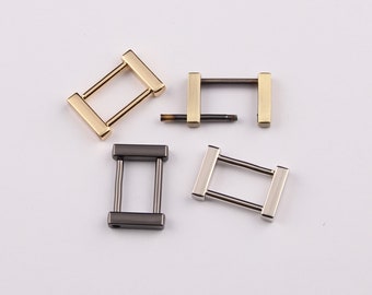 May include: Four metal D-ring buckles in different finishes: gold, silver, black, and antique brass. The buckles are rectangular with a small opening in the center.