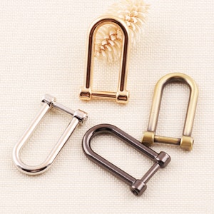May include: Three metal D-rings in different finishes: gold, silver, and black. The rings are all the same size and shape, and they are arranged in a semi-circle.