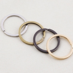 Peut inclure: Quatre porte-clés métalliques de couleurs argent, laiton, bronze foncé et or. Les anneaux sont ronds et ont une ouverture fendue pour attacher des clés ou d'autres articles. Les porte-clés sont disposés de manière légèrement superposée.