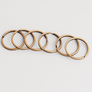 Peut inclure: Six anneaux de porte-clés en laiton antique sont disposés en rangée sur un fond blanc. Chaque anneau est circulaire avec une petite ouverture, suggérant qu'ils peuvent être ouverts et fermés. Les anneaux sont en métal.