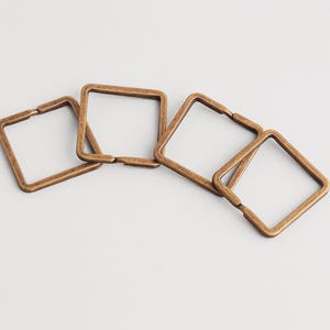 May include: Four bronze-coloured square metal rings are displayed on a white background. The rings are linked together at one corner. These decorative rings are suitable for crafting and jewellery making.