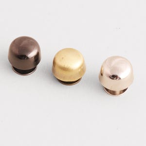 May include: Three metal dome-shaped rivets in different colors: dark brown, gold, and rose gold. These rivets have a rounded top and a flat base, suitable for various crafting projects.
