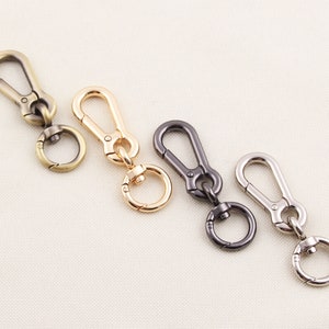 May include: Four metal swivel clasps in antique brass, gold, gunmetal, and silver. Each clasp has a spring-loaded hook and a small ring. The clasps are arranged in a row against a neutral background.