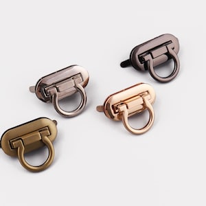 May include: Four metal purse clasps in various finishes: silver, bronze, gold, and gunmetal. Each clasp features a rectangular body with a hinged ring for closure. The clasps are displayed on a white surface.