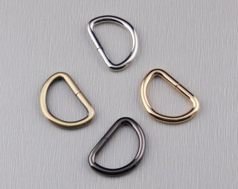 May include: Four D-shaped metal rings in different finishes: silver, gold, brass, and black.