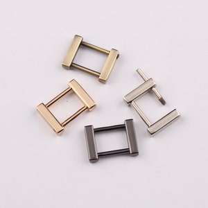 Puede incluir: Cuatro hebillas metálicas rectangulares en varios acabados: dorado, bronce, plateado y negro. Cada hebilla tiene un marco rectangular con dos barras paralelas que conectan los lados. Probablemente para correas de bolsos u otros accesorios.