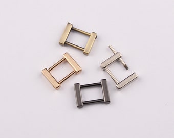 May include: Four metal rectangle-shaped buckles in various finishes: gold, bronze, silver, and black. Each buckle has a rectangular frame with two parallel bars connecting the sides. These are likely used for bag straps or other accessories.