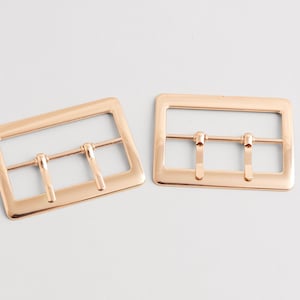 Può includere: Due fibbie in metallo color oro rosa. Ogni fibbia ha una cornice rettangolare con tre barre. Le fibbie sono progettate per essere utilizzate in vari progetti di artigianato e cucito. Le fibbie sono in metallo lucido.